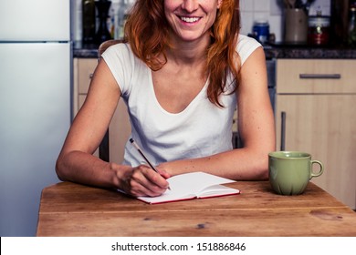 Happy woman writing in her kitchen - Powered by Shutterstock