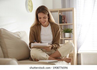 Happy woman writing letter while sitting on sofa at home