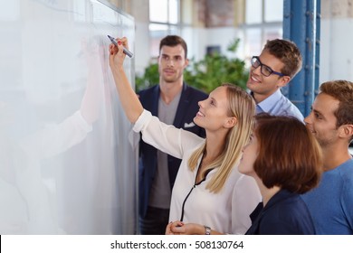 Happy Woman Writing On Blank White Board With Fellow Staff Members Standing Around Smiling