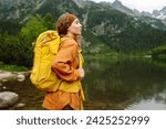 Happy woman with a yellow hiking backpack enjoying the mountain landscape.  Adventure, travel, sport, active life.