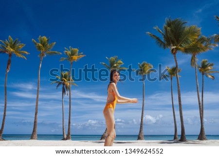 A happy woman in a yellow swimsuit runs in the sand with palm trees on the island   