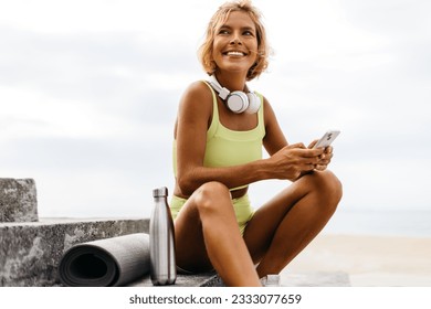 Happy woman in yoga attire uses her smartphone after a great yoga workout on the promenade stairs, enjoying the seaside serenity and the refreshment from her exercise routine. - Powered by Shutterstock