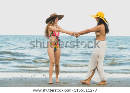 Happy women in bikinis dance together on tropical sand beach in summer vacation. Travel lifestyle.