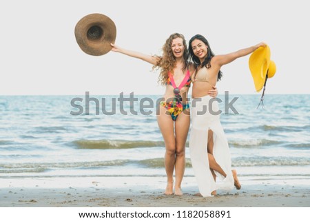 Happy women in bikinis dance together on tropical sand beach in summer vacation. Travel lifestyle.