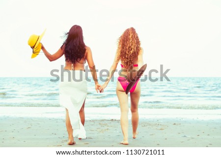 Happy women in bikinis go sunbathing together on tropical sand beach in summer vacation. Travel lifestyle.