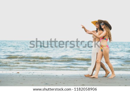 Happy women in bikinis go sunbathing together on tropical sand beach in summer vacation. Travel lifestyle.