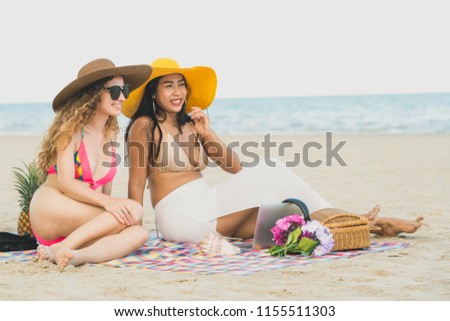 Happy women in bikinis sitting together on tropical sand beach in summer vacation. Travel lifestyle.