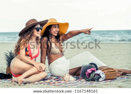 Happy women in bikinis sitting together on tropical sand beach in summer vacation. Travel lifestyle.