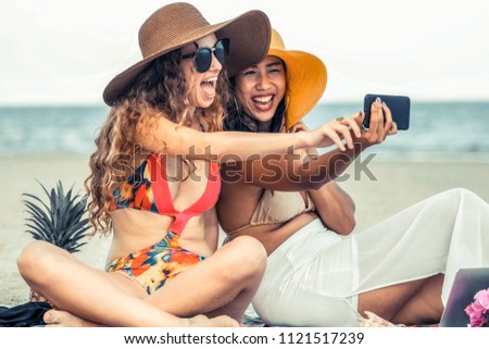 Happy women in bikinis taking selfie photograph from mobile phone together on tropical sand beach in summer vacation. Travel lifestyle.