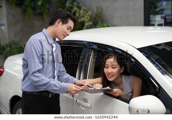 Happy women customer with car dealer\
agent making deal and signing on agreement document . Auto Leasing\
Business.                                          \
