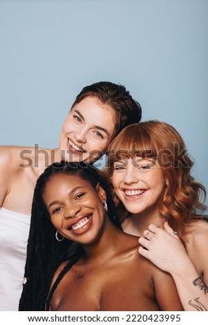 Happy women with different skin tones smiling at the camera in a studio. Group of body confident young women embracing their natural beauty. Three body positive young women standing together.