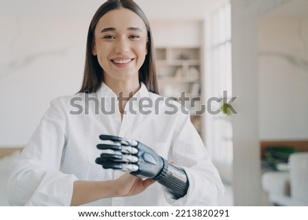 Happy women with disability enjoying using bionic prosthetic arm at home. Smiling young woman satisfied with artificial limb, high tech prosthesis. Lifestyle of people with disabilities.