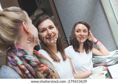 Happy women enjoying a coffee in a cafe in Copenhagen. They are in their twenties, laughing and talking each other. Smart casual clothing.