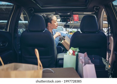Happy Women Full Paper And Tote Shopping Bags In Cart.Colorful Bag And Brown Box In Back Car Trunk Storage.Woman Checking And Setting The Product She Bought. Shopping Addiction Or Shopaholic Concept.