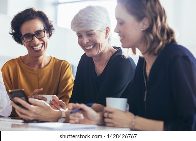 Happy women having casual talk and looking at mobile phone during break. Three businesswomen during break at office. - Powered by Shutterstock