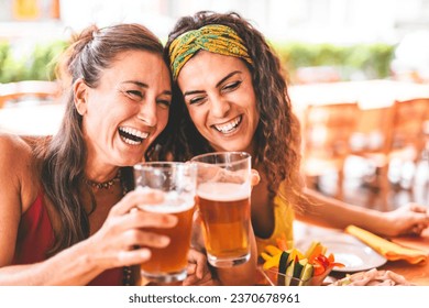 Happy women having fun drinking beer outdoors at pub terrace, Two girls friends toasting glass of pint at brewery pub enjoying food, Social Lifestyle concept with happy young people - Powered by Shutterstock