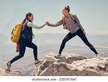 Happy women help while hiking up a rocky mountain in nature with backpack. Females friends exercise in nature park climbing and jumping while with sportswear training or trekking together outdoors