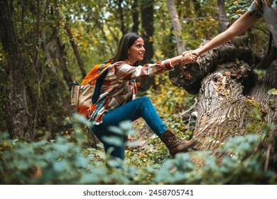 Happy women help while hiking up a rocky mountain in nature with backpack. Females friends exercise in nature park climbing and jumping while with sportswear training or trekking together outdoors - Powered by Shutterstock