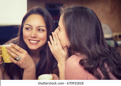 Happy women whispering and drinking coffee. Smiling girls telling secrets and gossiping. 