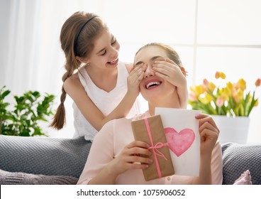 Happy Women's Day! Child Daughter Is Congratulating Mom And Giving Her Postcard And Gift. Mum And Girl Smiling And Hugging. Family Holiday And Togetherness.