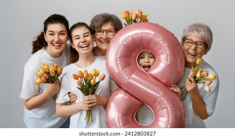 ¡Feliz día de la mujer! Las hijas están felicitando a mamá y a las abuelas dándoles tulipanes de flores. Grannys, mamá y niñas sonriendo con fondo gris claro. Vacaciones familiares y unión.