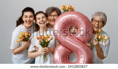 Happy women's day! Children daughters are congratulating mom and grandmothers giving them flowers tulips. Grannys, mom and girls smiling on light grey background. Family holiday and togetherness.