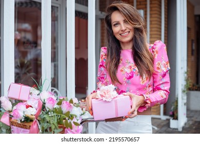 Happy Wonderful Lady Standing Outdoors Near Large Basket Of Fresh Roses And With Smile Holding In Hands Beautiful Present Box. Theme Pink Party, Celebration, Holiday, Gift, Flower Composition, Decor