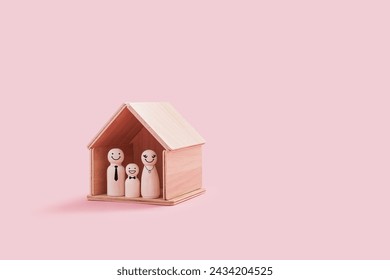 Happy wooden family figures inside a tiny wooden house isolated on a pink background. Parent and smiling kid stand close together