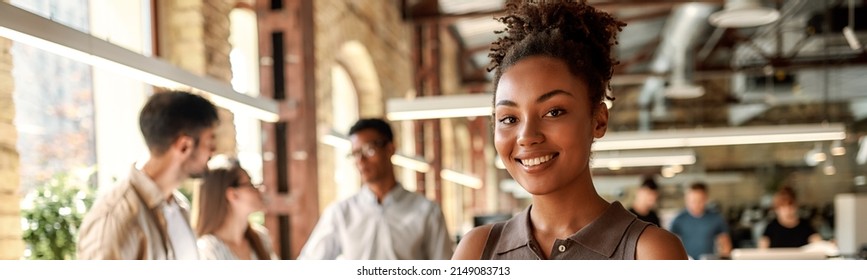 Happy To Work Here. Young And Cheerful Afro American Woman Holding Laptop And Smiling While Standing In The Modern Office.