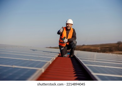 A happy worker is crouching next to installed solar panels and approving eco life.