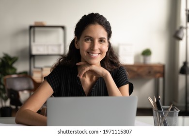 Happy worker. Headshot portrait of confident young latin female posing by office computer at work desk. Smiling successful millennial woman remote employee freelancer sit at workplace look at camera