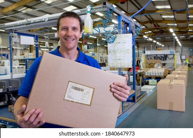A happy worker holding and showing the final packaged box picked up from the assembly line in a large factory