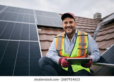 Happy worker using digital tablet during solar panels maintenance and looking at camera.