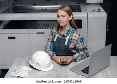 Happy Worker Young Woman In Uniform Production Workplace Laptop. Background CNC Laser Machine For Wood. Concept Small Business Craftsman.