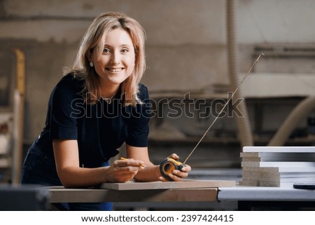 Happy worker young woman working in wooden furniture workshop, DIY marking dimensions of product.