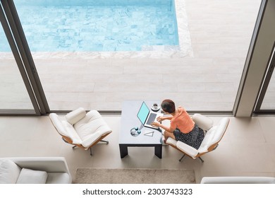 Happy working senior digital nomad woman sitting with laptop at luxury pool villa near beach, Phuket Thailand. - Powered by Shutterstock