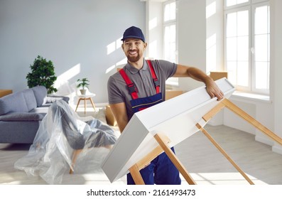 Happy workman carrying furniture. Moving company or truck delivery service worker removing things from old house or apartment. Strong young man in workwear uniform carrying modern table and smiling