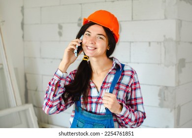 happy workwoman in blue overall mature talking on mobile phone on brick wall background on construction site - Shutterstock ID 2254761851