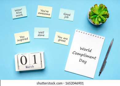 Happy World Compliment Day. Office desk with plant, notebook, pen and paper slips with compliments text for office worker such as GOOD JOB. Calendar date 1 March, greeting card. Flat lay, top view