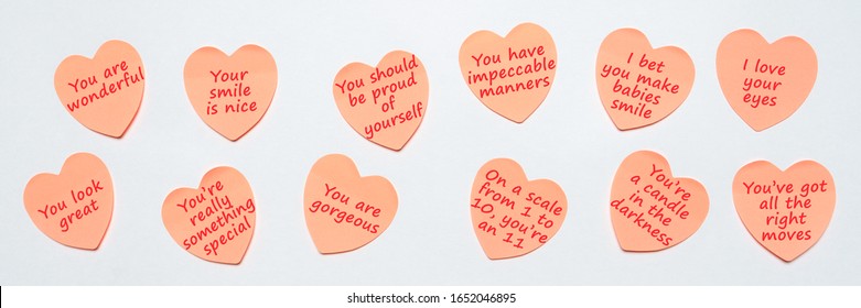 Happy World Compliment Day. Pink paper stickers in heart shape with text of popular compliments for beautiful lady pasted on white background. Greeting card for world compliment day. Flat lay, banner