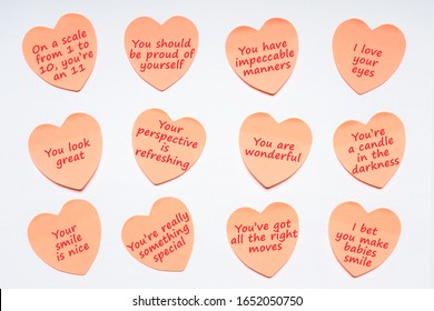 Happy World Compliment Day. Pink paper stickers in heart shape with text of popular compliments for beautiful lady pasted on white background. Greeting card for world compliment day 1 March. Flat lay
