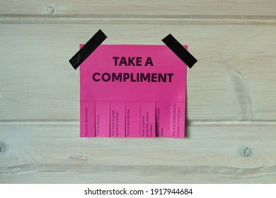 Happy World Compliment Day. Take a compliment. Pink wall paper sticker with text of popular compliments for beautiful lady pasted on wooden background. Creative concept.