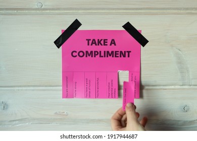Happy World Compliment Day. Take a compliment. Pink wall paper sticker with text of popular compliments for beautiful lady pasted on wooden background. Creative concept.
