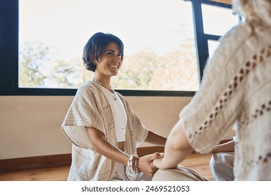 Happy yoga coach holding hands of woman during women group holistic healing session. Mindful ladies sitting in circle meditating together doing breathing exercises giving support at body care training - Powered by Shutterstock