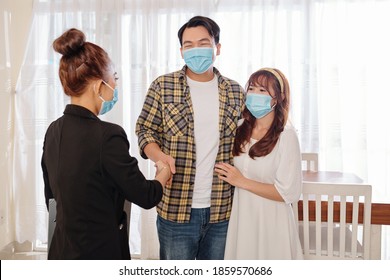 Happy Youg Asian Couple In Medical Masks Meeting With Real Estate Agent In New House