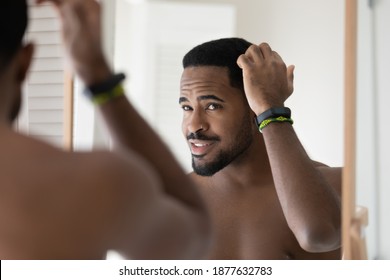 Happy Young 30s Handsome African American Bare Man Looking In Mirror, Styling Hair With Fingers, Getting Ready For Dating Or Preparing For Workday After Morning Showering Procedures In Bathroom.