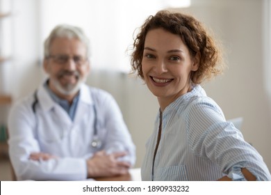 Happy Young 30s Woman Looking At Camera With Smiling Older Senior Male Doctor On Background. Female Patient Satisfied With Checkup Meeting Or Medical Healthcare Service In Clinic, Feeling Healthy.