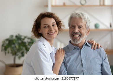 Happy Young 35s Female Physician Doctor Cuddling Shoulders Of Smiling Older Retired Patient, Looking Together In Distance. Dreamy Pleasant Nurse Caregiver Supporting Elderly Mature Man At Home Visit.