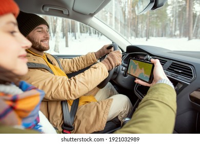 Happy Young Active Man In Warm Winterwear Looking At Map On Screen Of Smartphone Held By His Wife While Driving During Winter Travel