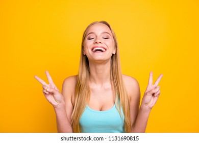 So happy! Young and adorable blond girl happily laughs and demonstrating two fingers v-sign isolated on yellow background